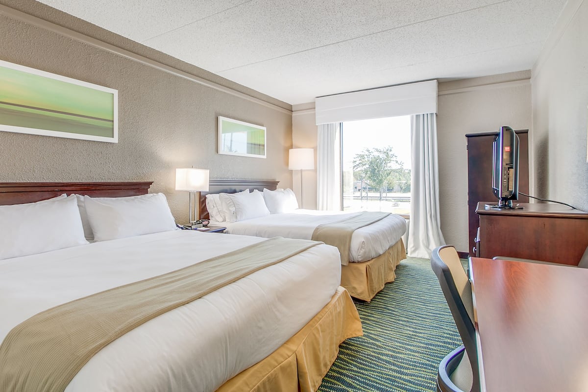 A hotel room with two beds, a desk, a chair, a TV, and artwork on the walls.