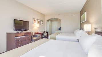 A hotel room with two beds, a television, a desk with a chair, and a small table with a lamp.