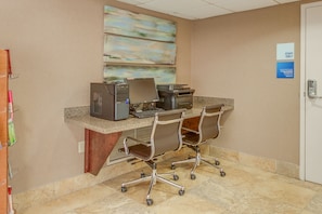 Un espacio de trabajo en un hotel, con un escritorio, dos sillas de oficina, una computadora e impresora.