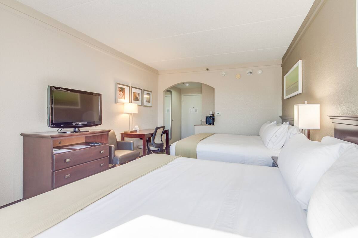 A hotel room with two beds, a desk with a television, a chair, and a desk lamp.