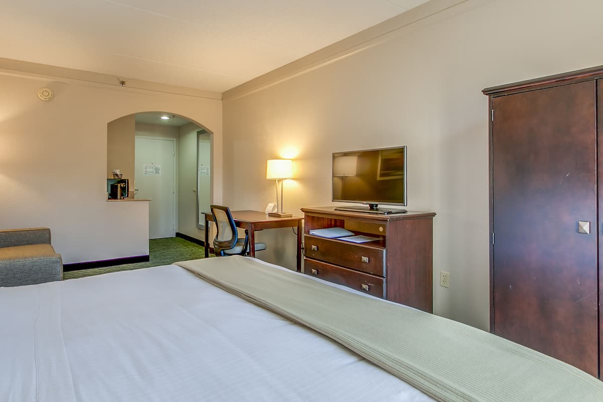 A hotel room with a large bed, a desk with a computer, a chair, a wardrobe, and a TV.
