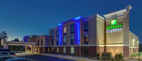 Un hotel Holiday Inn Express con una fachada moderna, múltiples accesos y un estacionamiento.