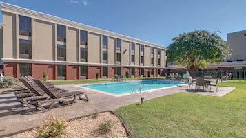 A hotel with a swimming pool, lounge chairs, and a fenced outdoor area.