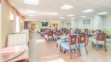 A spacious dining area with multiple tables and chairs, a television mounted on the wall, and a patterned wall design.