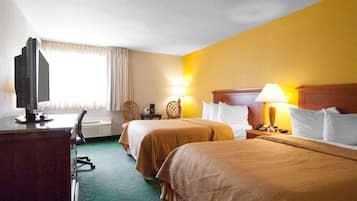 Habitación de hotel con dos camas, un escritorio con computadora, una silla, una lámpara y una ventana con cortinas.