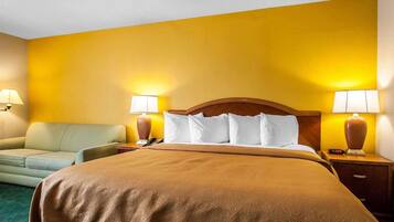 Quarto de hotel com uma cama grande, duas luminárias de cabeceira, uma mesa de cabeceira, um sofá e um abajur na parede.