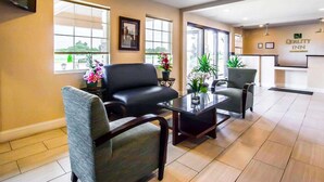 A hotel lobby with a reception desk, two armchairs, a coffee table, and large windows with potted plants. - Quality Inn Cairo I-57 (Cairo)