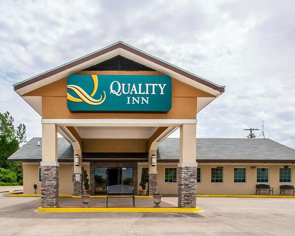 A Quality Inn hotel entrance with a covered walkway, stone pillars, and a bench.