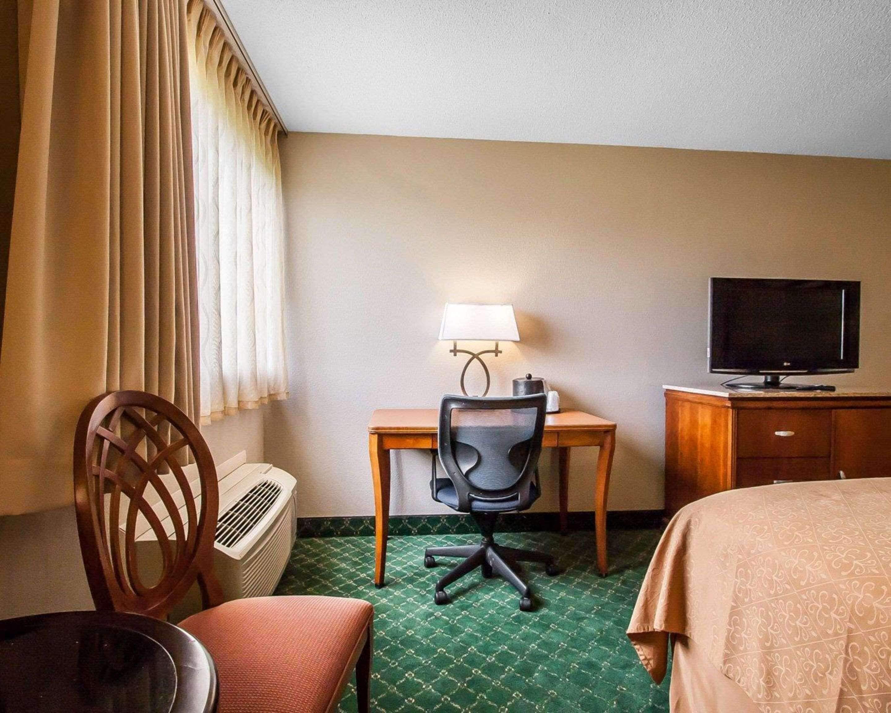 Une chambre d’hôtel comprenant un lit, un bureau avec une lampe, une télévision, une chaise et un radiateur.