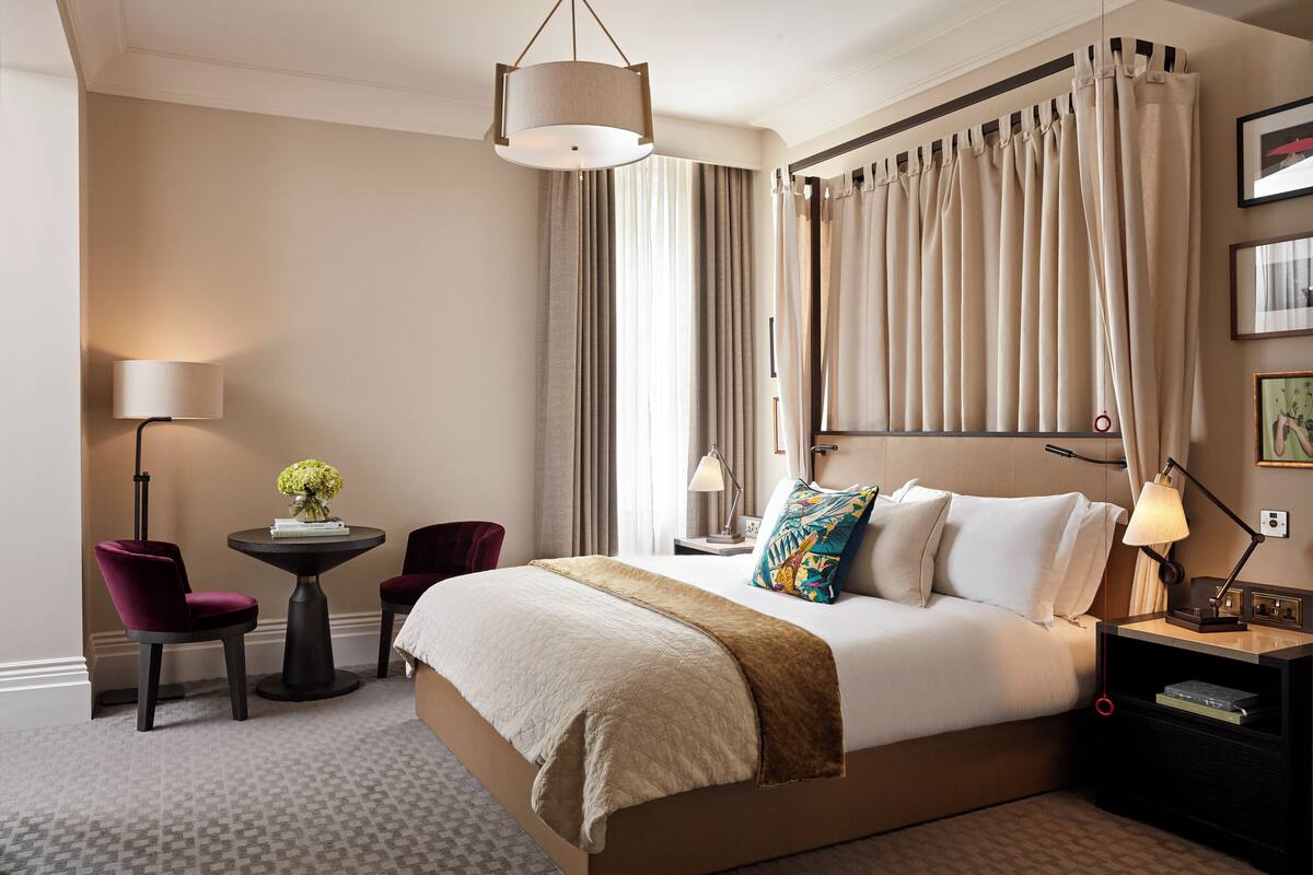 A hotel room with a large bed, a bedside table with a lamp, a small round table with a chair, and a decorative vase.