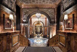 A grand hallway with marble columns, a chandelier, and a patterned floor leading to a room with a large window. - Kimpton Fitzroy London by IHG (London)