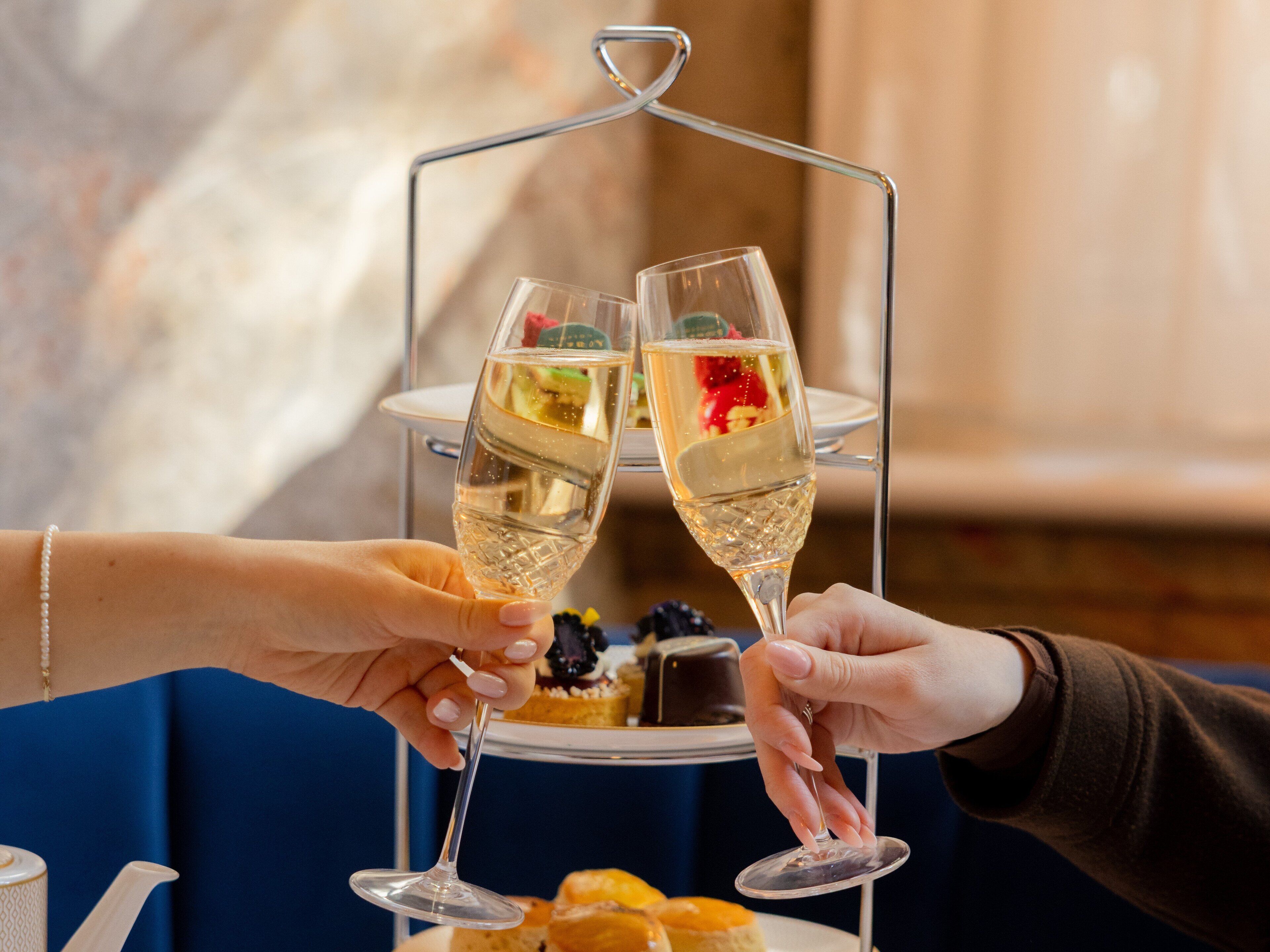 Zwei Personen stoßen mit Champagnergläsern auf einem Tisch mit einer Dessertplatte an.