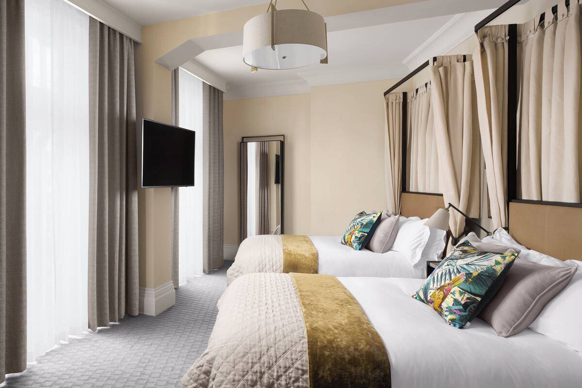 A hotel room with two beds, a flat-screen TV, a large mirror, and a view of the outdoors.
