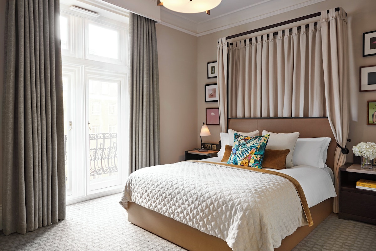 A hotel room with a large bed, a nightstand, a bedside table, a lamp, and a window with curtains.