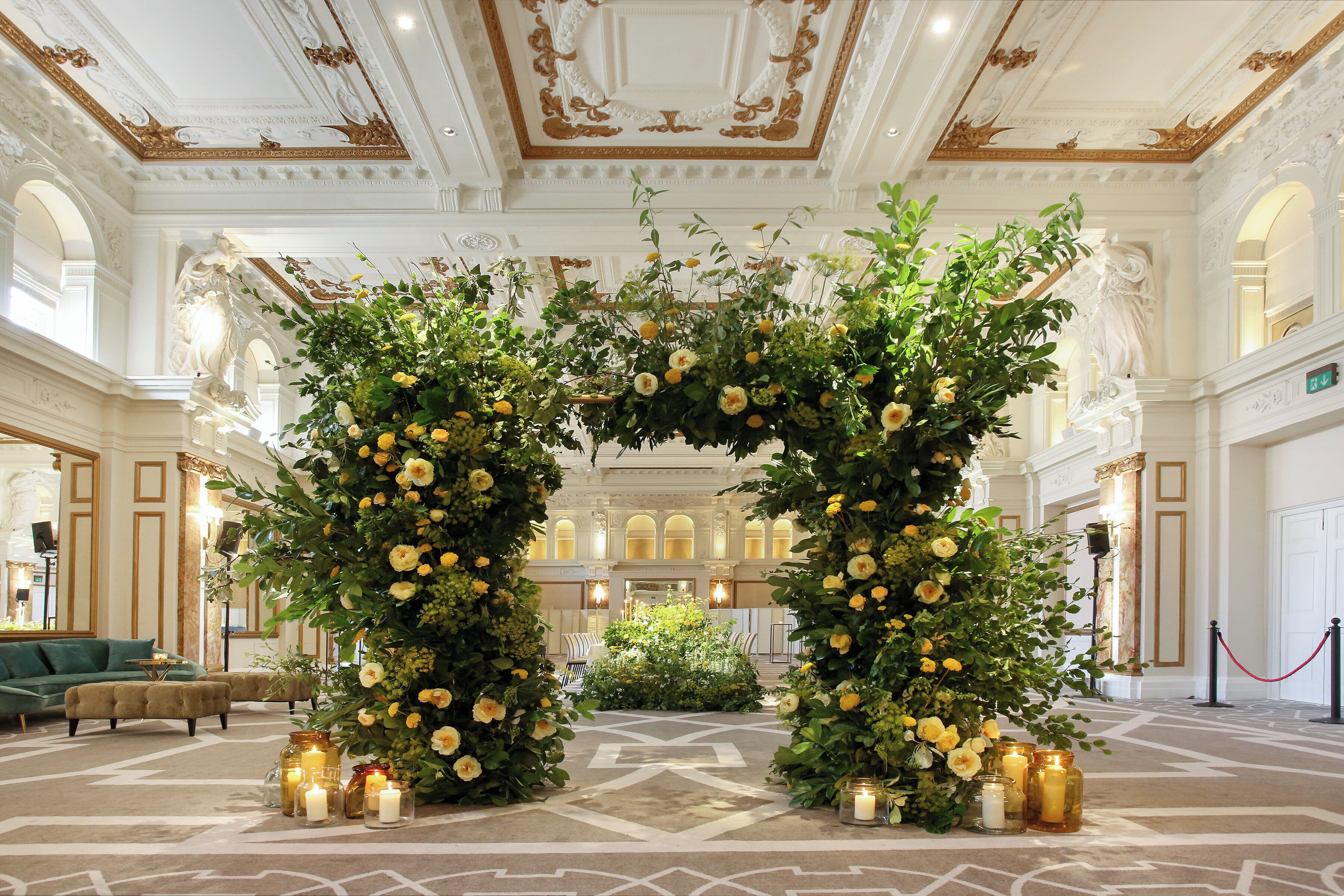 An ornate hall with a floral archway, chandeliers, and a patterned carpet.