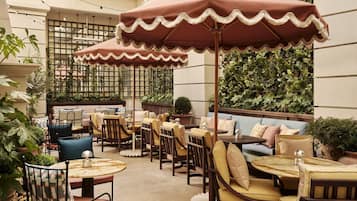 A cozy outdoor seating area with tables and chairs, surrounded by greenery and a decorative umbrella.