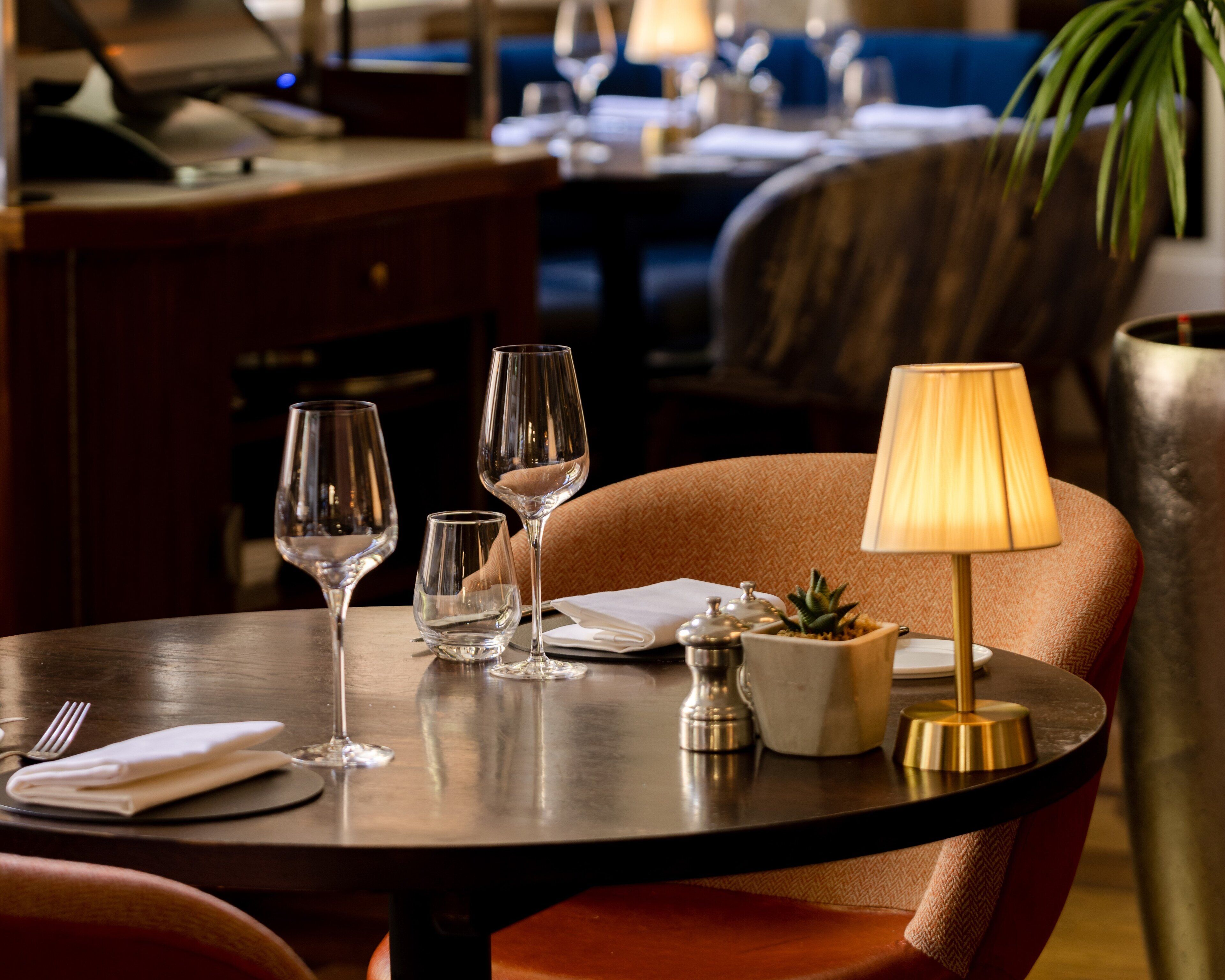 A dining table with wine glasses, a lamp, a small plant, and a napkin.