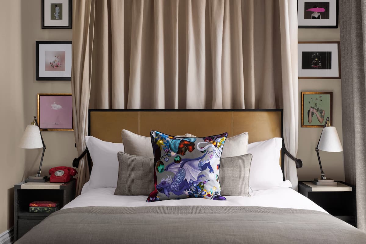 A neatly made bed with a colorful pillow, a headboard, and two bedside tables with lamps and a red telephone.