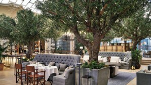 Eine großzügige Innenlounge mit einem großen Baum, bequemen Sitzgelegenheiten und einer Bar.