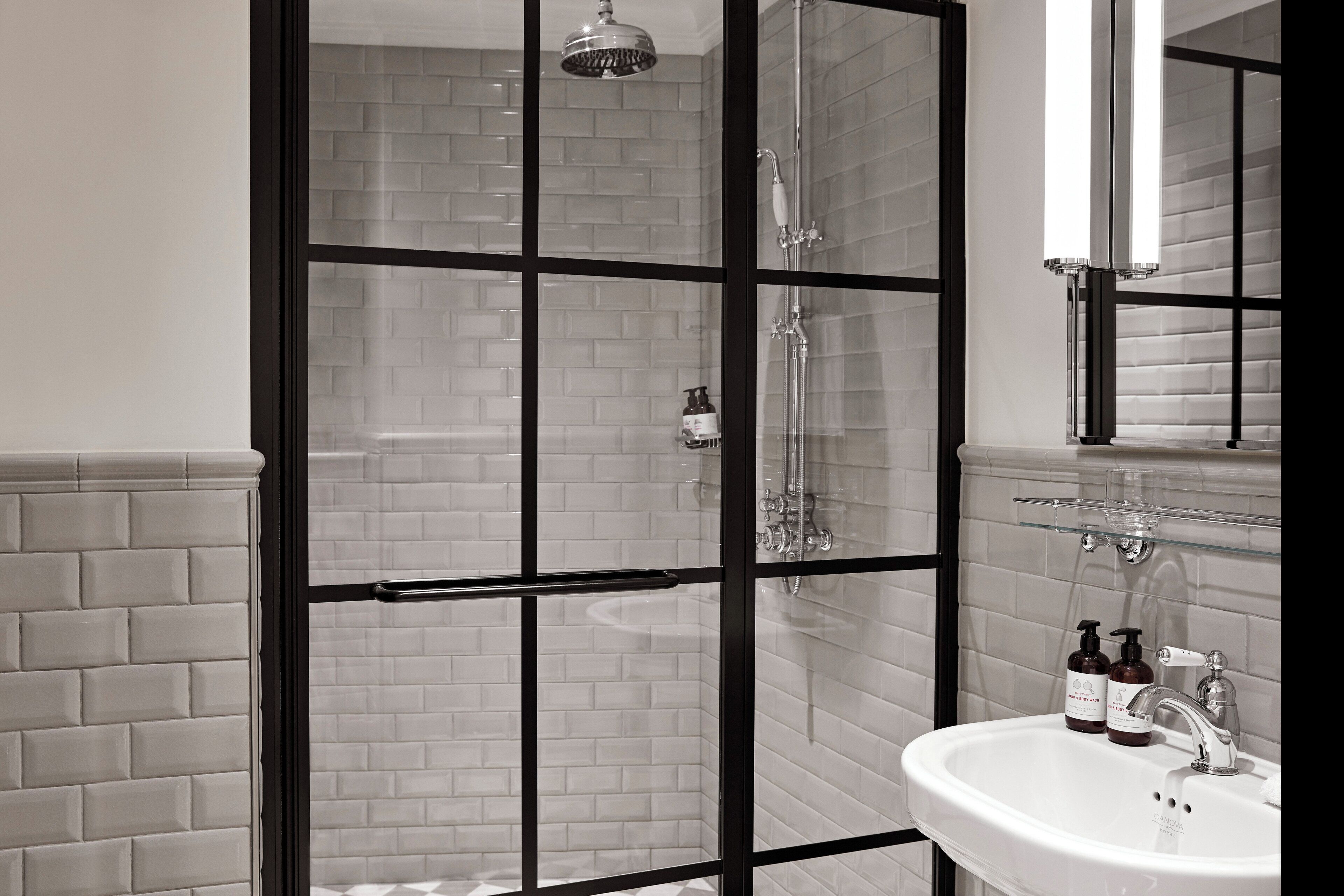 A modern bathroom with a glass-enclosed shower, a white sink with a mirror above it, and toiletries on the sink.