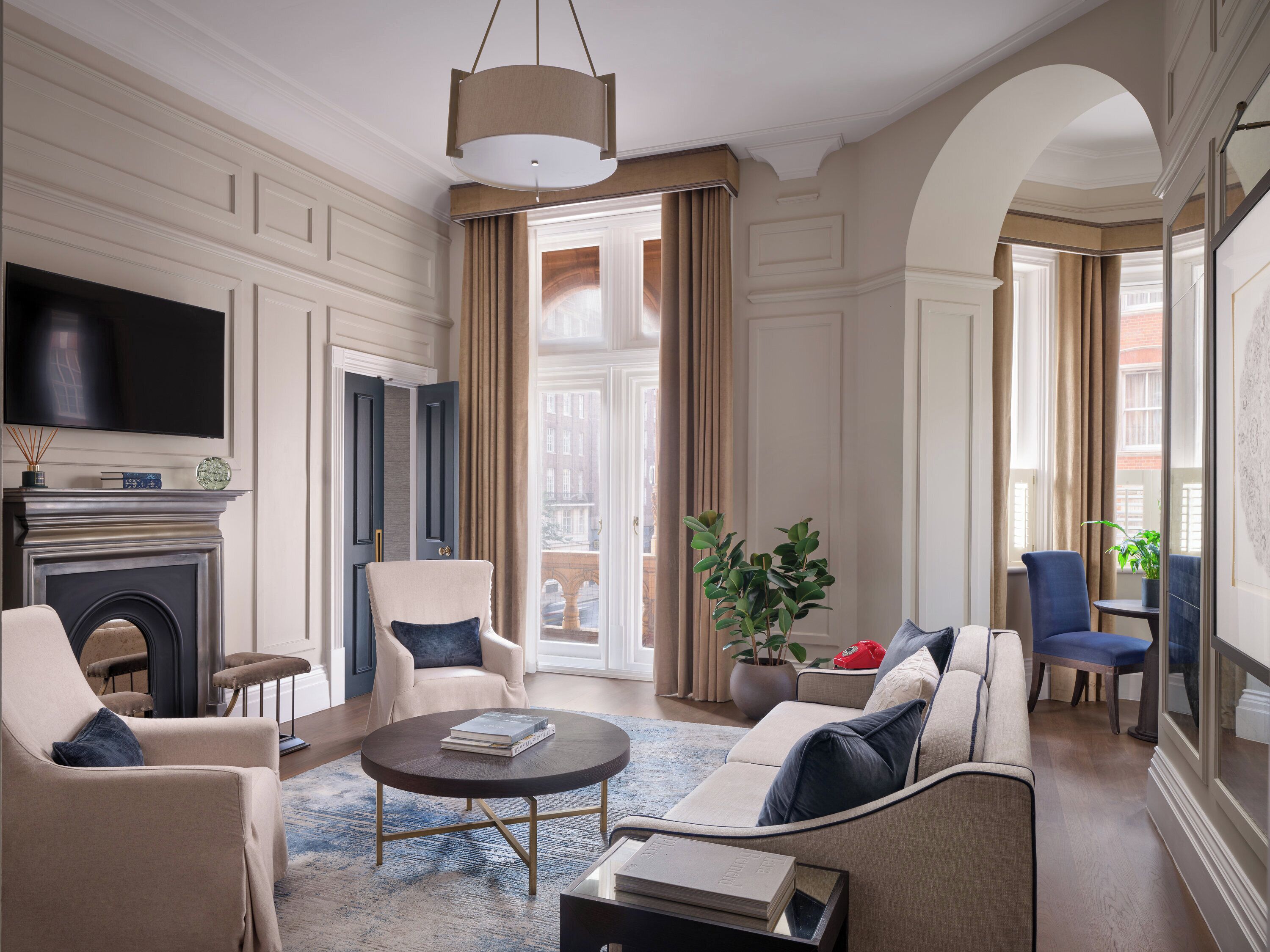 A spacious living room with a fireplace, comfortable seating, a television, and a large window offering a view of the city.