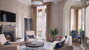 A spacious living room with a fireplace, comfortable seating, a television, and a large window offering a view of the city.
