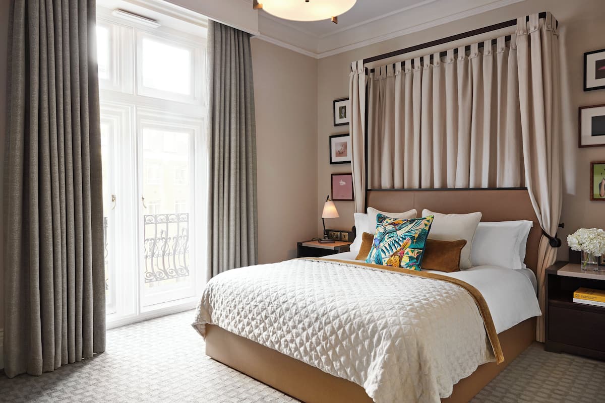 A hotel room with a large bed, a nightstand, a lamp, and a view of the outside.