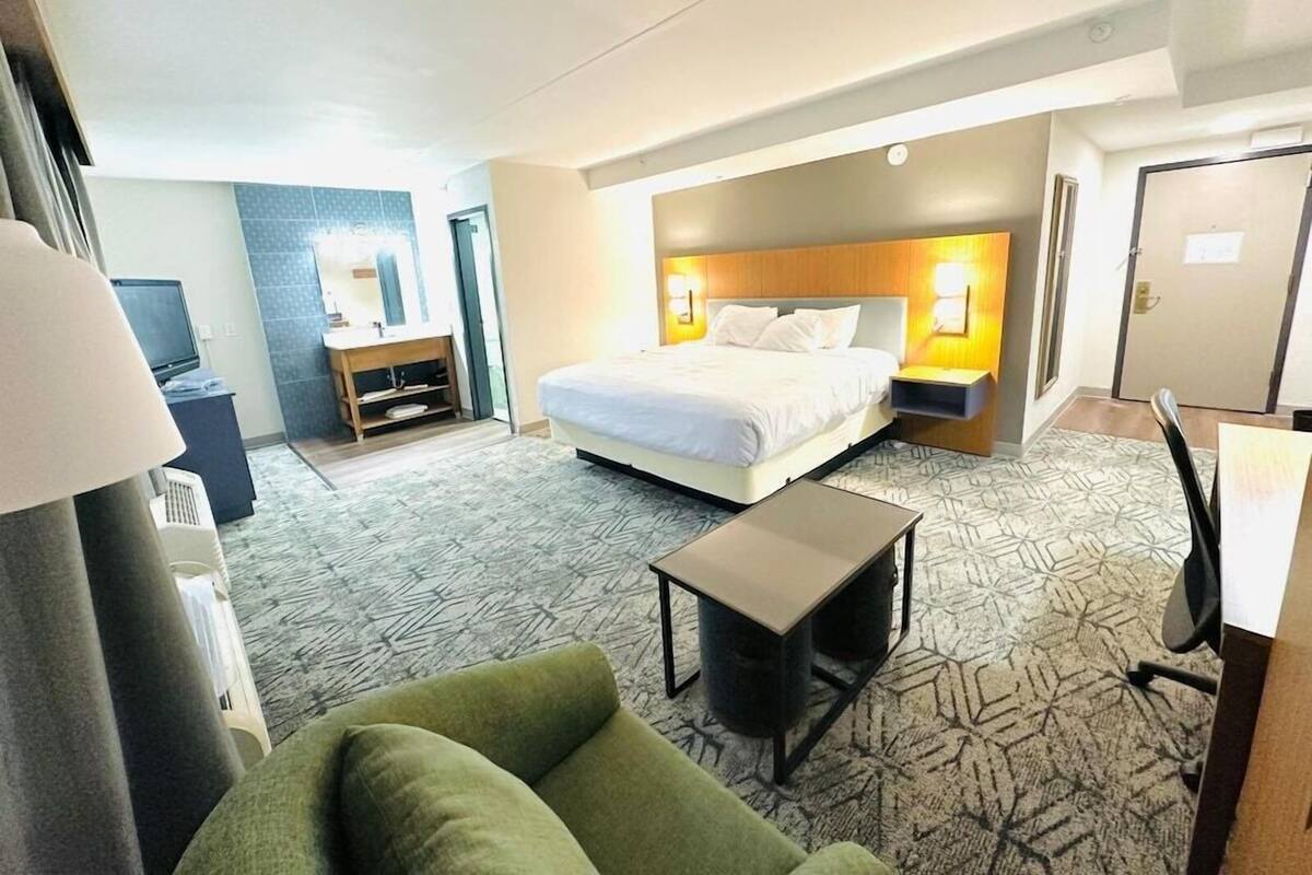 Ett hotellrum med en säng, sänglampor, ett skrivbord, en stol och en tv.
