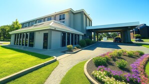 A modern building with a covered entrance, a well-maintained lawn, and flower beds.