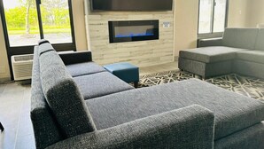 A modern living room with a large flat-screen TV mounted on a wooden wall, a built-in fireplace, and a sectional sofa.
