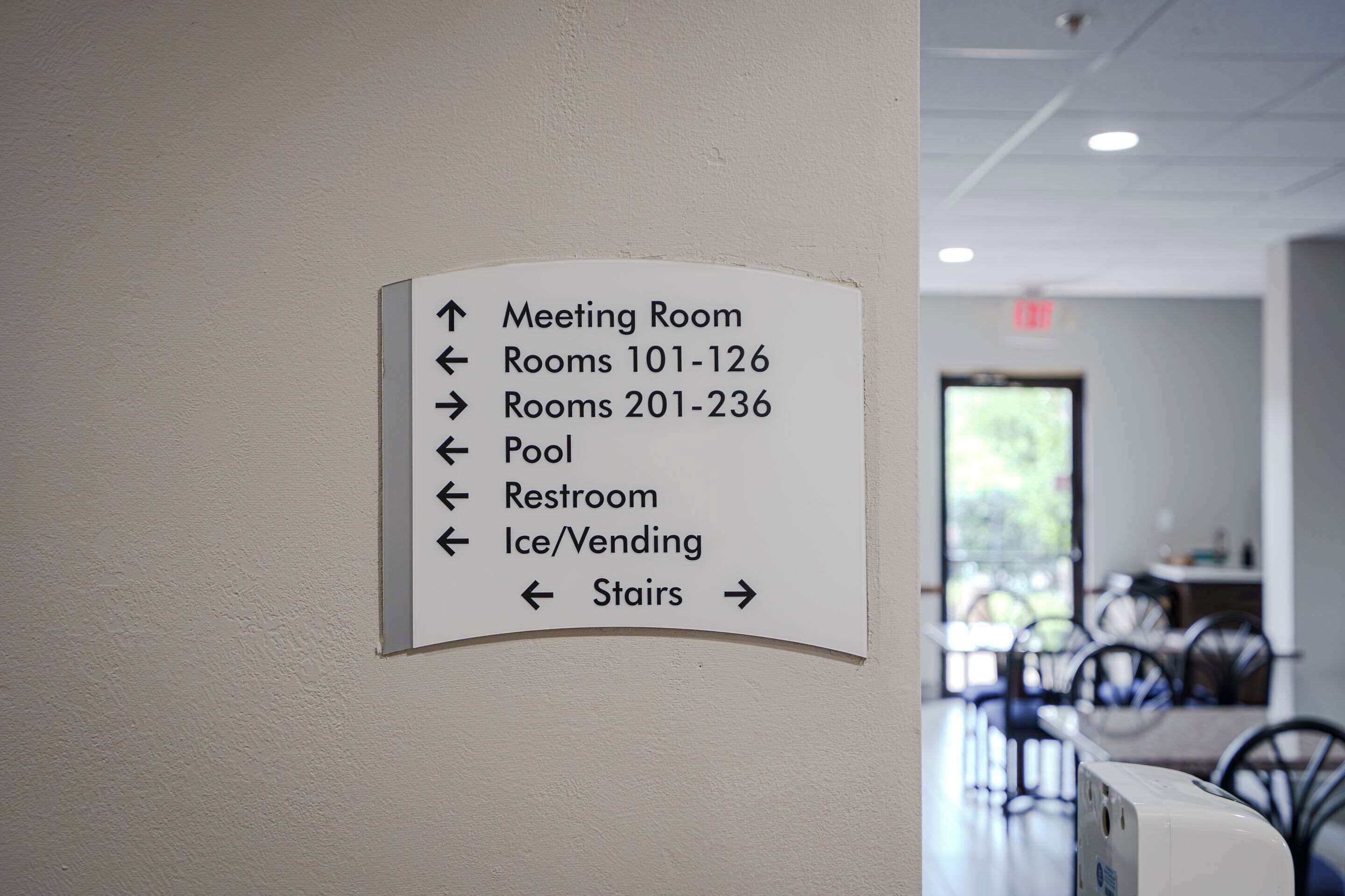 A directional sign in a hotel lobby indicating the locations of the meeting room, rooms 101-126, rooms 201-236, pool, restroom, ice/vending, and stairs.