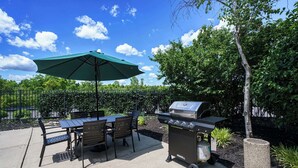 Eine Terrasse im Freien mit Grill, Tisch, Stühlen und Sonnenschirm.