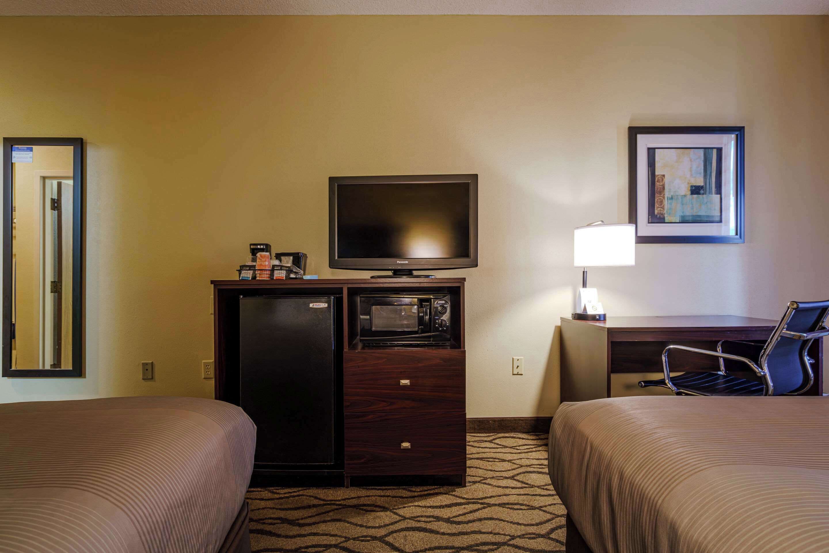 Habitación de hotel con dos camas, televisión, microondas, escritorio con lámpara y un cuadro en la pared.