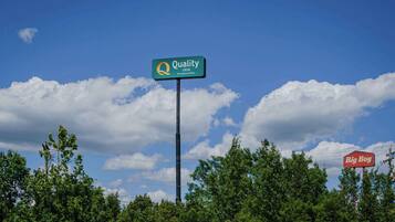 A Quality Inn sign with a clear blue sky and clouds in the background.