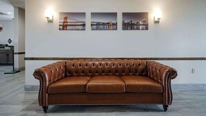 Ein braunes Ledersofa mit hoher Lehne und gepolsterten Zwickeln, platziert in einem Raum mit weißer Wand und drei gerahmten Fotografien darüber.