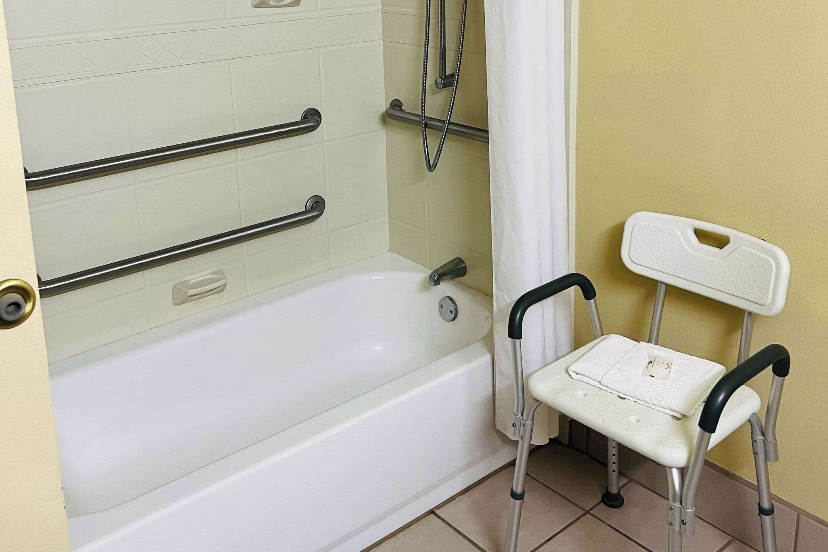 A bathroom with a bathtub, grab bars, a showerhead, and a wheelchair.