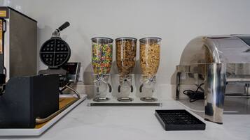 A waffle maker, three dispensers with different cereals, and a coffee machine on a kitchen counter.