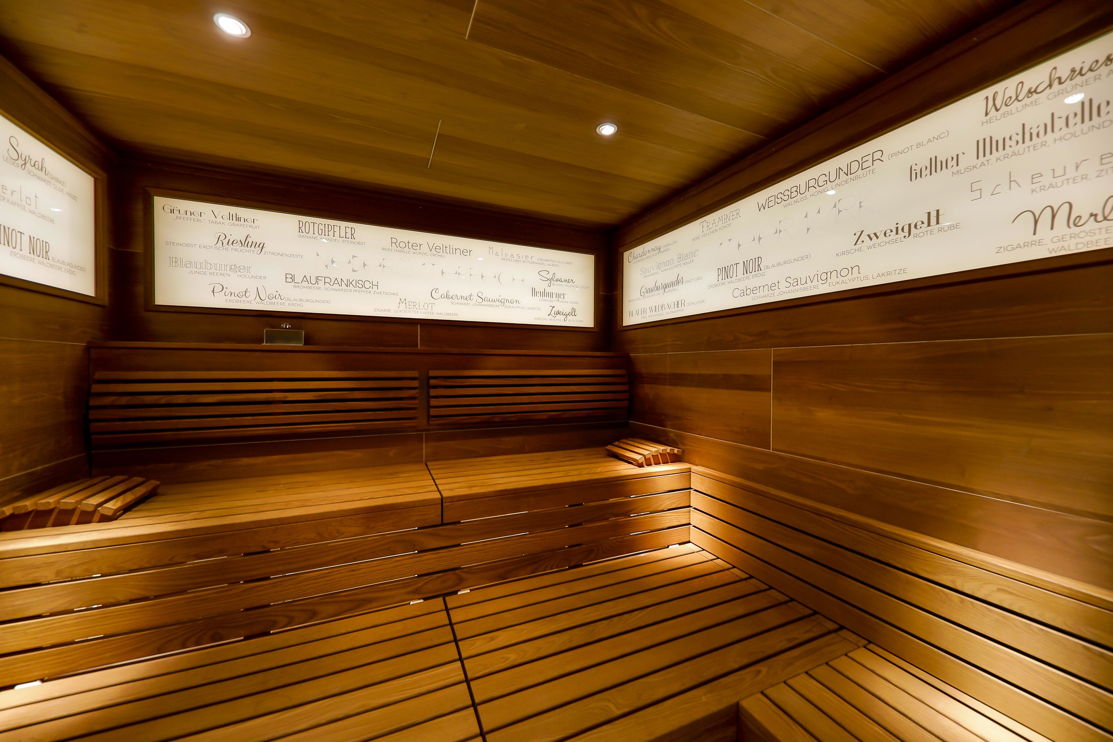 A sauna with wooden benches and walls displaying various wine names.