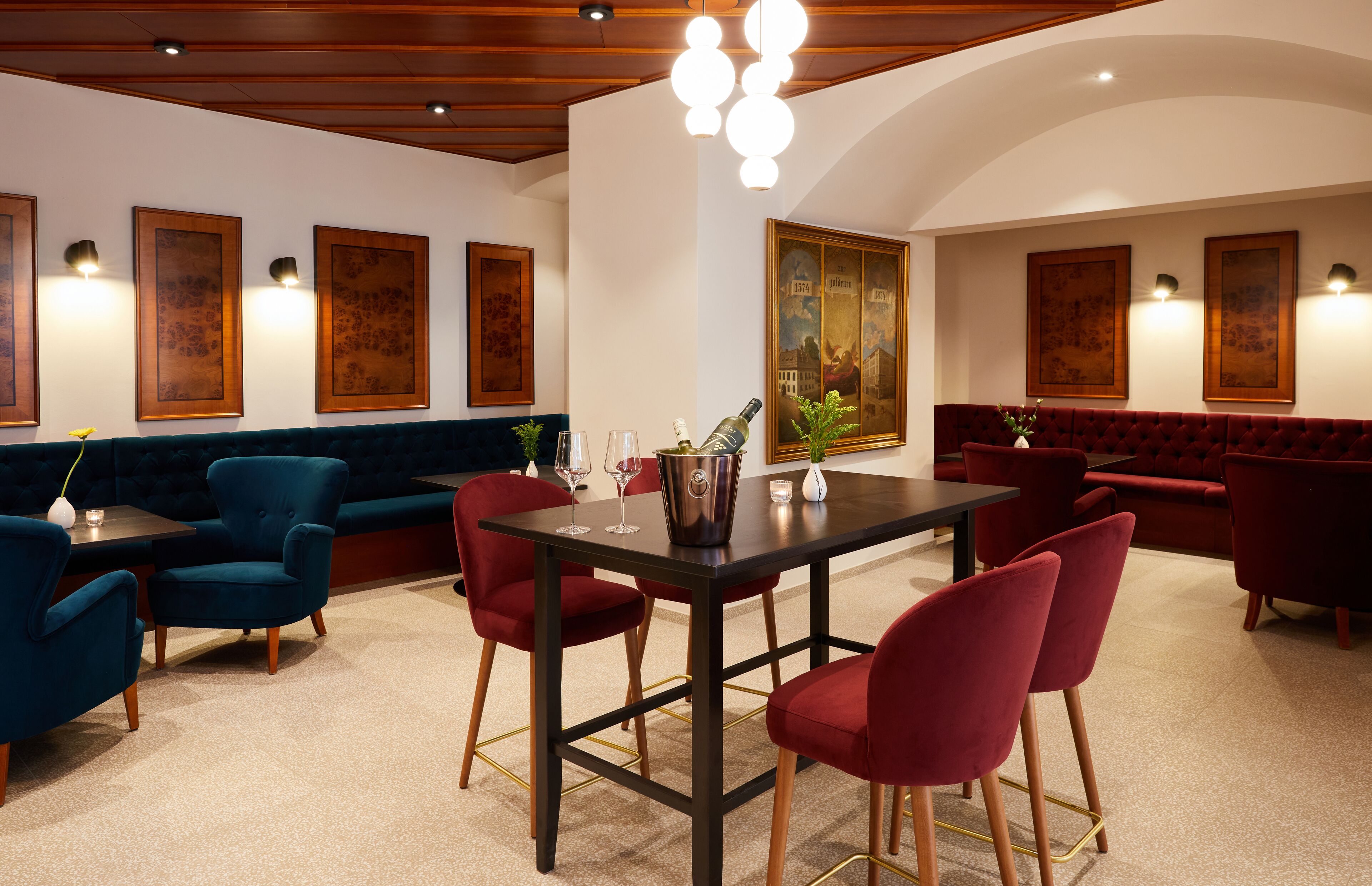 A dining area with a black table, red chairs, and a blue sofa. There are framed artworks on the walls and a chandelier above the table.