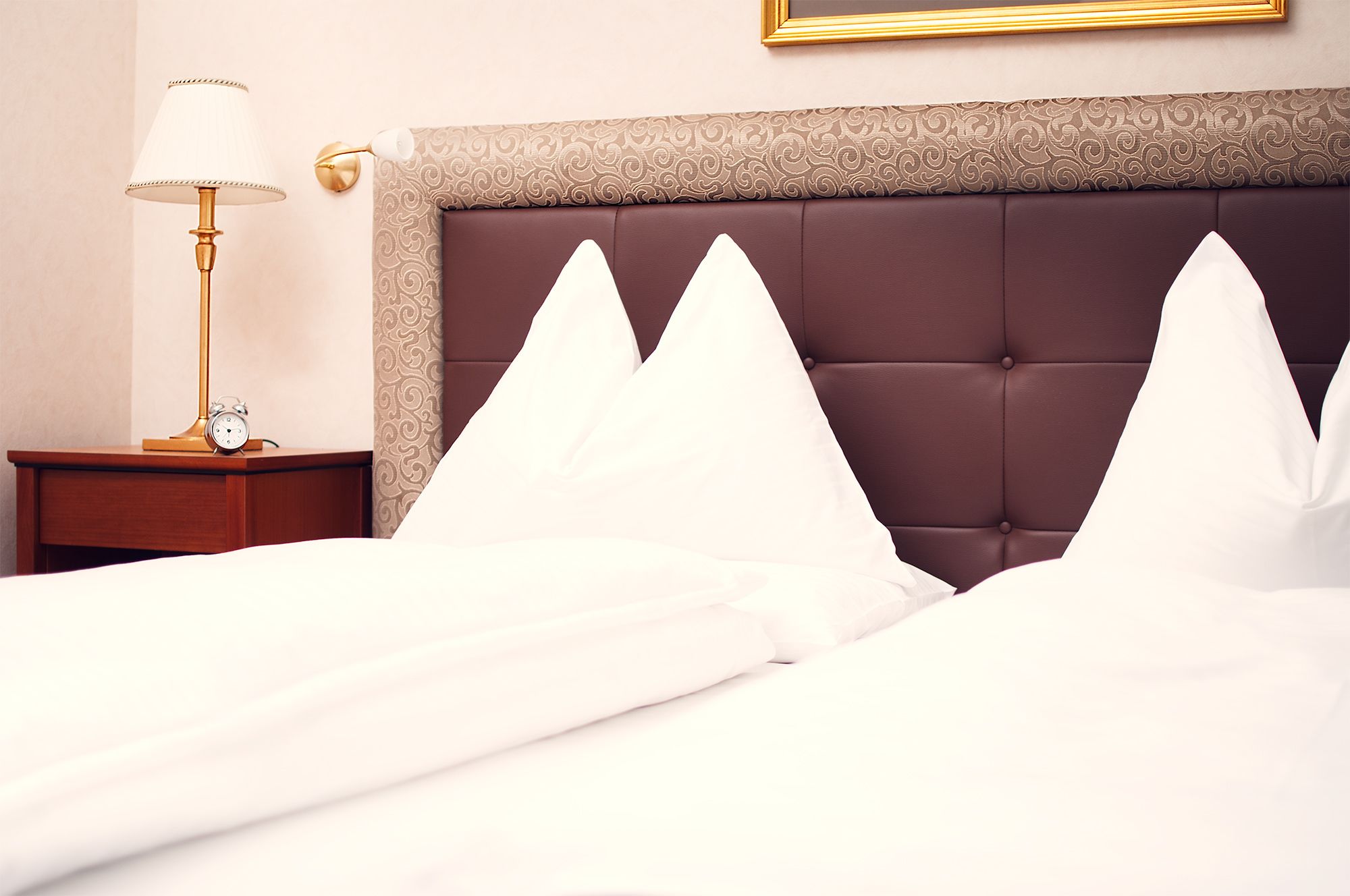 Una cama bien hecha con almohadillas blancas y un cabecero marrón.
