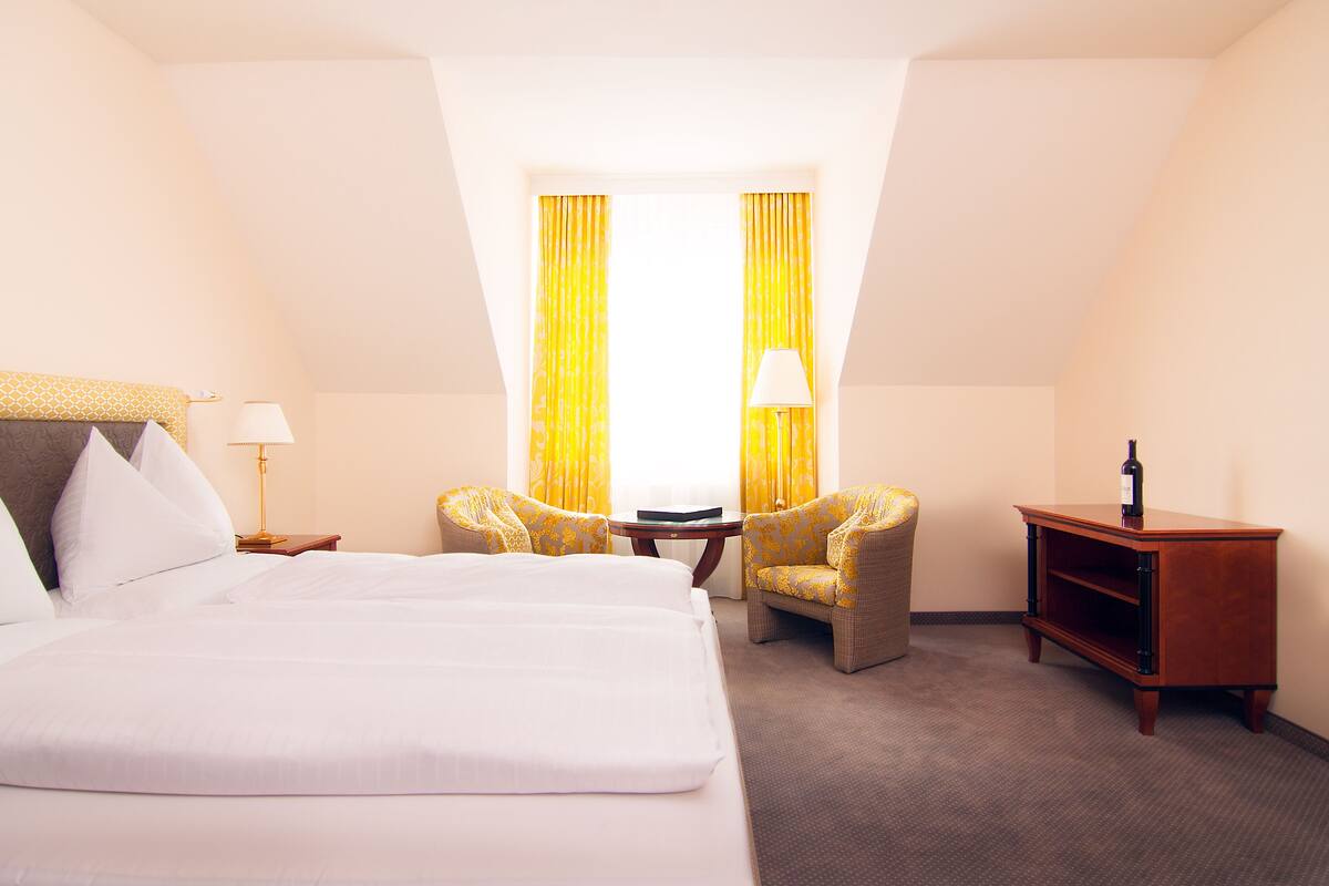 Ein Hotelzimmer mit einem großen Bett, zwei Sesseln, einem kleinen Tisch und einem Nachttisch.