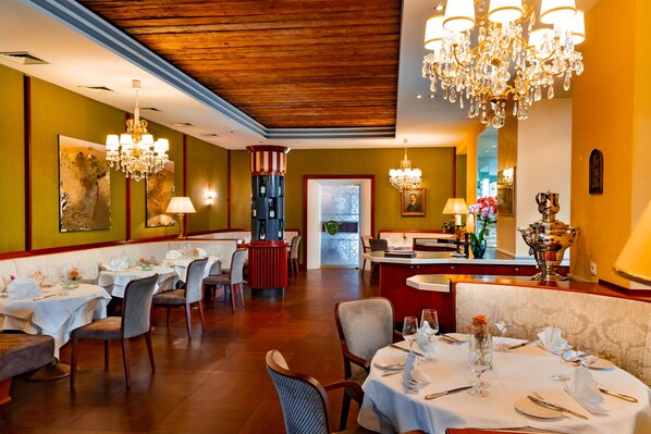 A restaurant with multiple dining tables, chandeliers, and a red column with a wine rack.