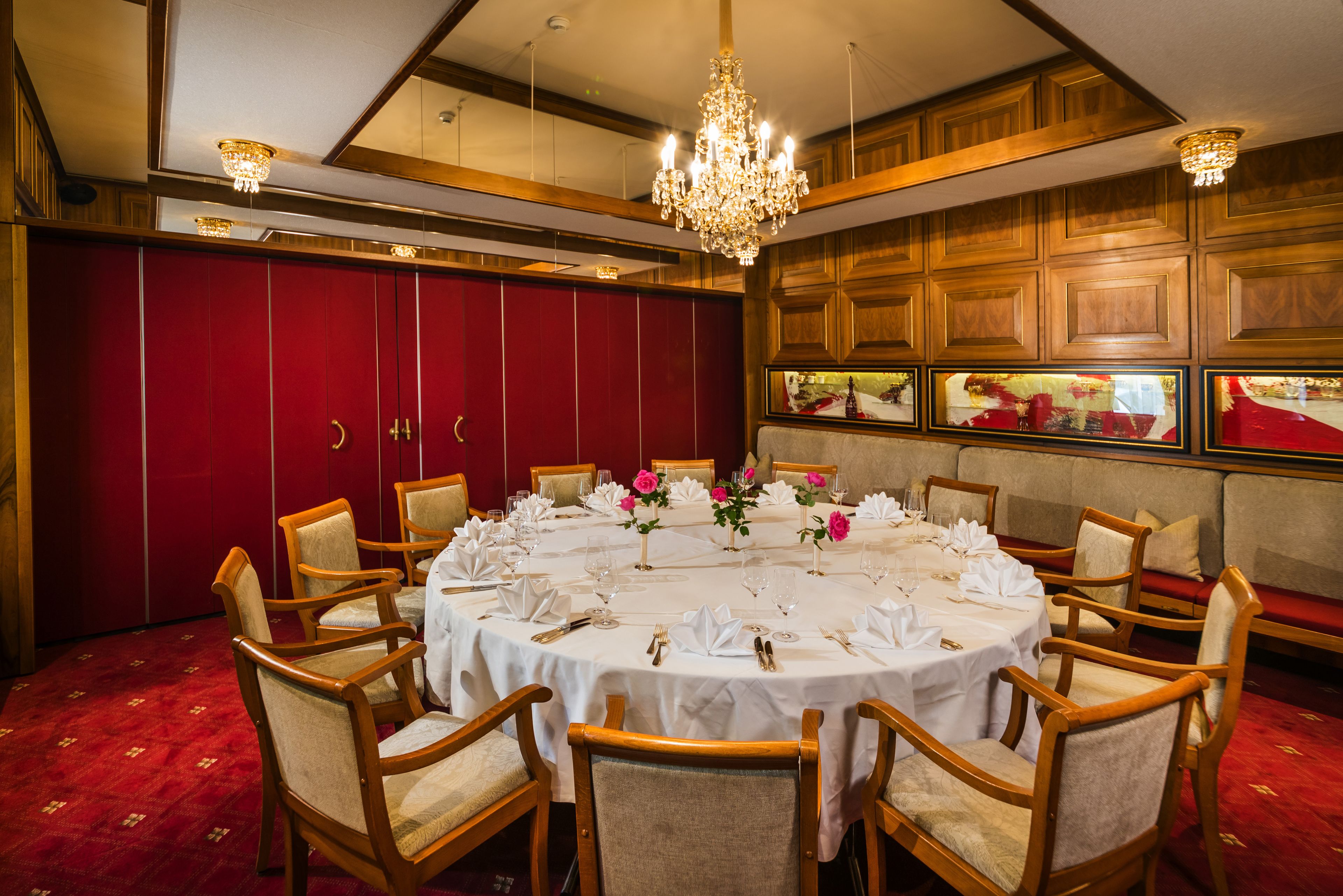 Um salão de festas com uma mesa redonda posta para um evento formal, rodeado por cadeiras de madeira.