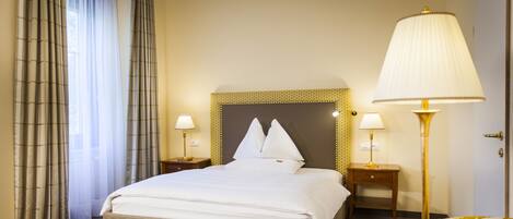 A hotel room with a large bed, two bedside tables with lamps, a sofa, and a patterned armchair.