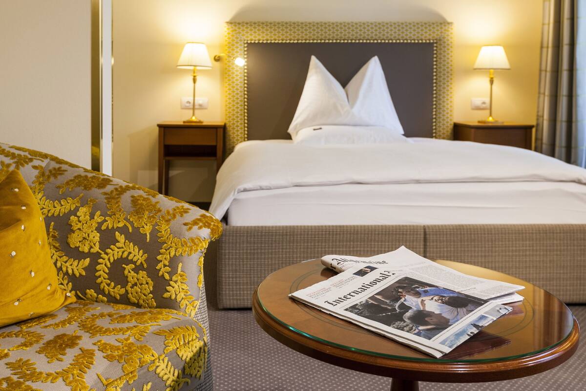 Ein Hotelzimmer mit einem Bett, einer Couch und einem runden Glastisch mit einer Zeitung.