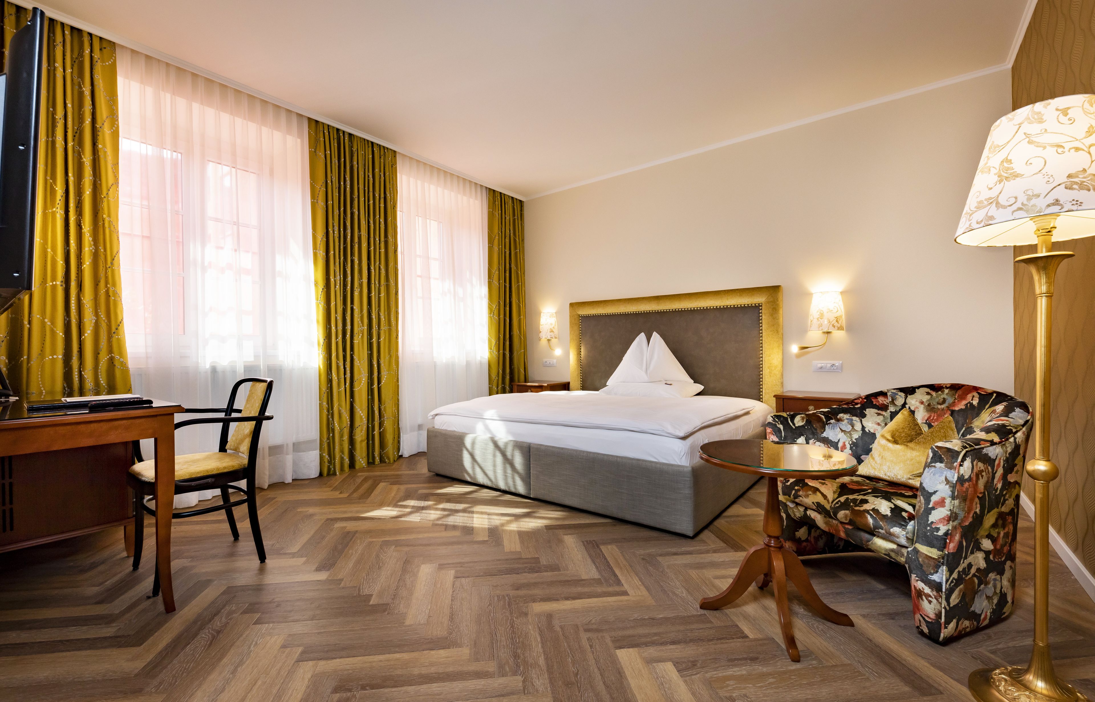 A hotel room with a bed, a desk with a chair, a small table, and a sofa.