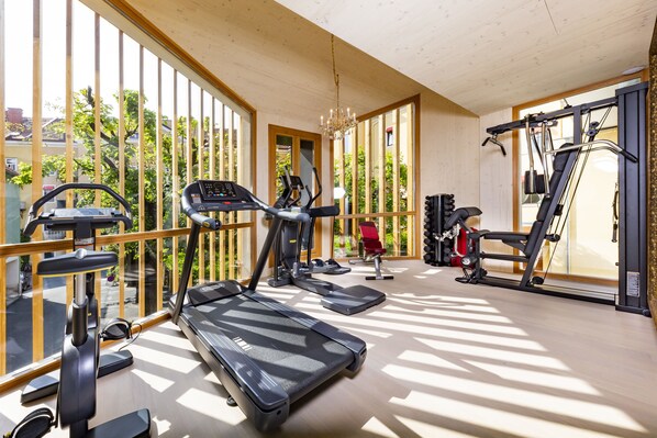 Un gimnasio doméstico bien iluminado con diversos equipos de ejercicio, ventanas amplias y una araña.