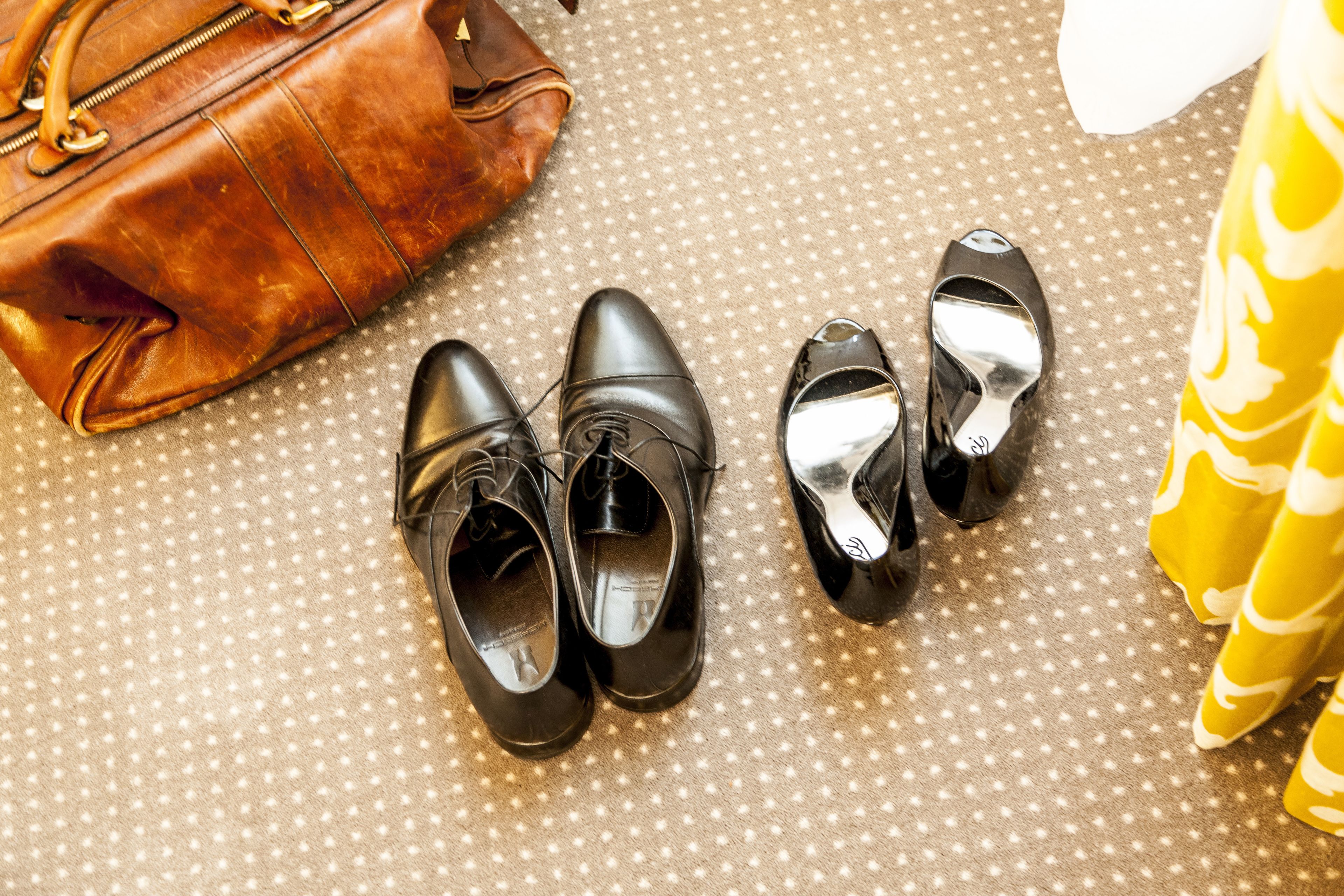 A pair of black shoes, a brown leather bag, and a yellow patterned fabric.