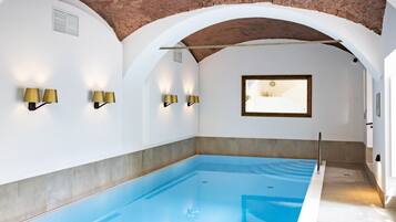 A swimming pool with a brick ceiling, white walls, and wall-mounted lighting.