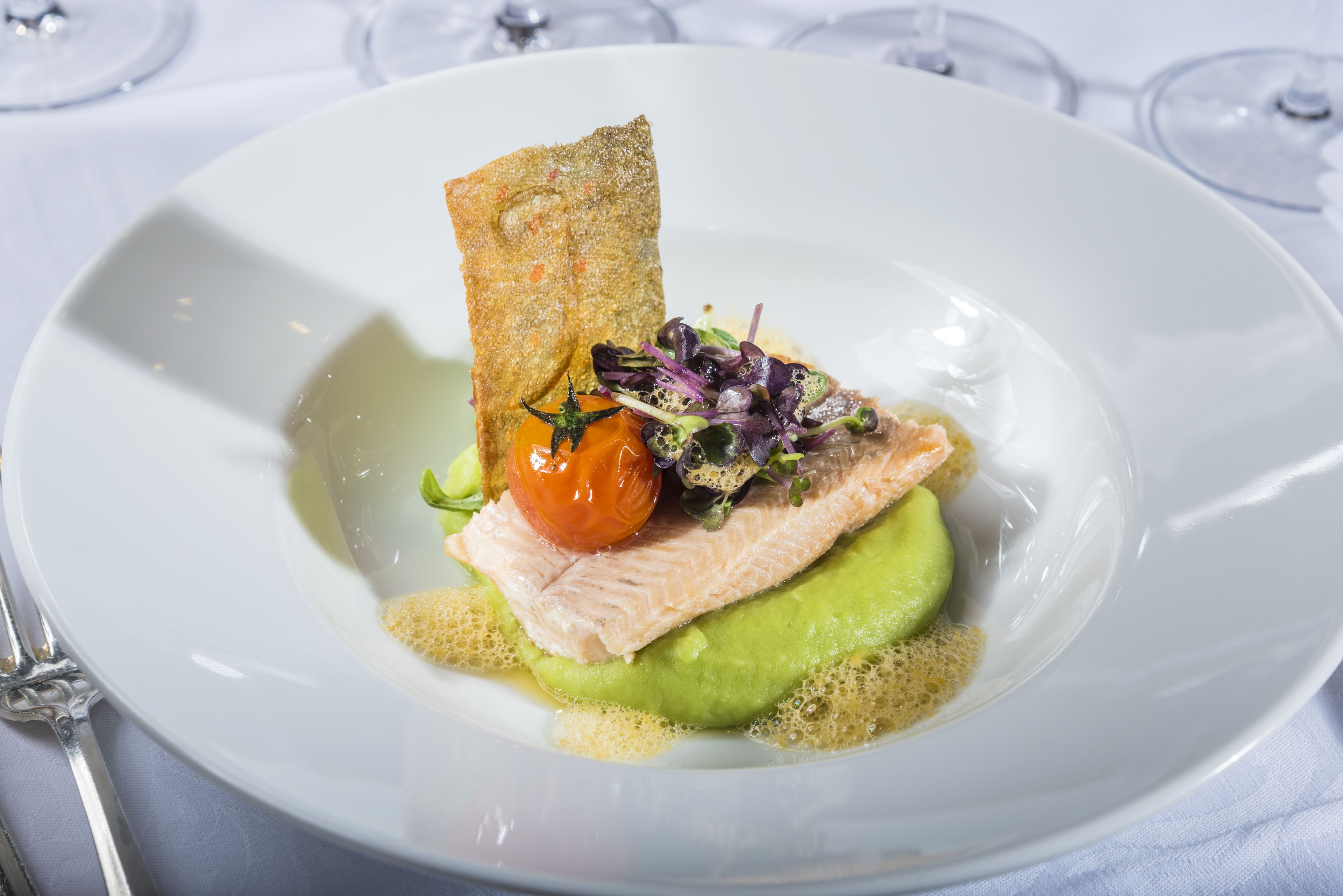 A white plate with a piece of salmon, a cherry tomato, and a piece of bread.